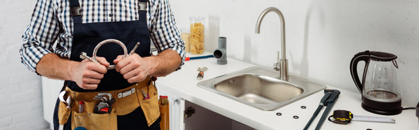 Панорамний урожай сантехніка в інструментальному поясі, що тримає металеву трубу на кухні
  - Фото, зображення