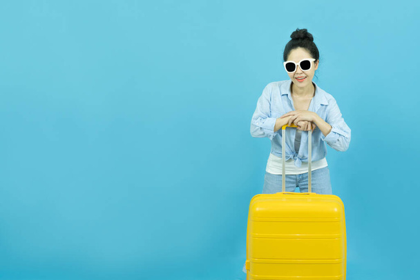 Summer holidays, vacation and travel concept.Traveler tourist beautiful young asian woman in casual clothes and sunglasses with yellow suitcase or luggage bag isolated on blue background. - Foto, Imagem