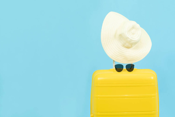 Summer holidays, vacation and travel concept.Yellow Suitcase or luggage bag with sun hat on blue background for copy space. - Φωτογραφία, εικόνα