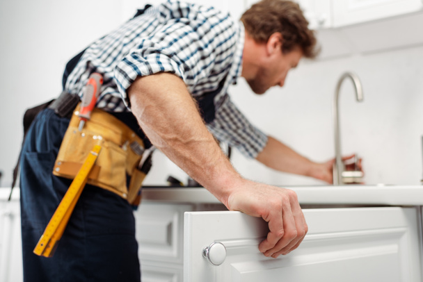 Selectieve focus van loodgieter in gereedschapsriem reparatie keukenkraan    - Foto, afbeelding