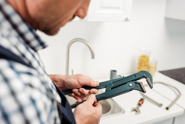 Cropped view of plumber holding pipe wrench in kitchen  - Foto, immagini