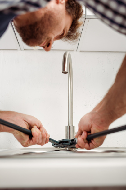 Selectieve focus van loodgieter holding pipe moersleutel tijdens de vaststelling van keukenkraan  - Foto, afbeelding