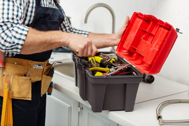 Cropped view of workman in overalls opening toolbox on kitchen worktop  - Photo, Image
