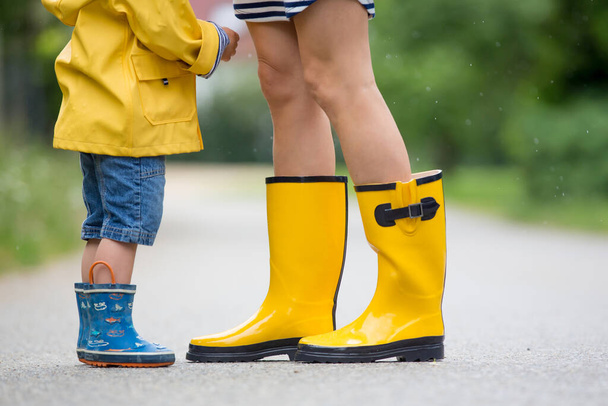 Mother and toddler child, boy, playing in the rain, wearing boots and raincoats - Fotoğraf, Görsel