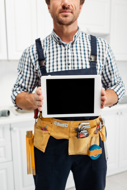 Vágott kilátás munkás overallban és szerszám öv tartó digitális tabletta üres képernyő a konyhában  - Fotó, kép