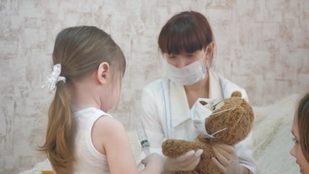 子供は病院で遊ぶ。ゲームは医者看護師獣医師ワクチンで患者を治療するふりをします。可愛い女の子がおもちゃのクマに注射。赤ちゃんは医療用のマスクで. - 映像、動画