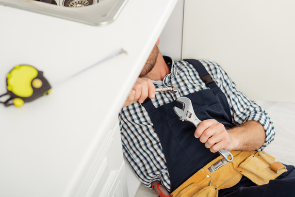 Boru anahtarı ve metal boruyla mutfak lavabosunu tamir eden seçici bir tesisatçı.  - Fotoğraf, Görsel