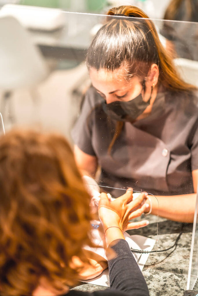 Manicure and pedicure salon, coronavirus, covid-19, social distance. The reopening due to the pandemic, security measures. Female worker with black mask in nail salon - Фото, зображення
