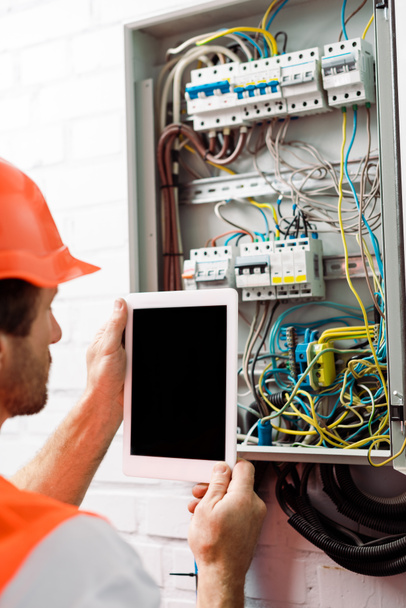 Selective focus of electrician holding digital tablet with blank screen near electrical distribution box - Photo, Image