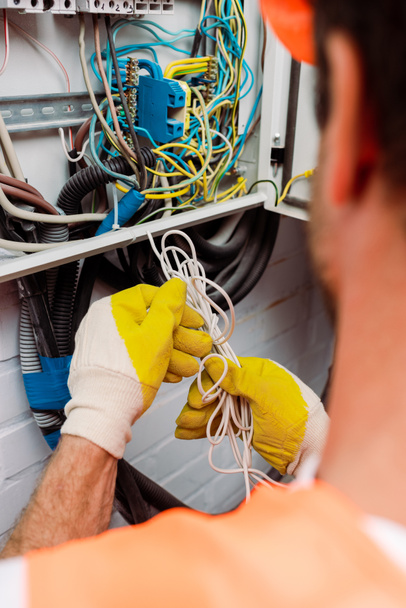 Elektrikçinin seçici odak noktası elektrik dağıtım kutusunu tamir ederken elinde kablolar tutan eldivenler. - Fotoğraf, Görsel
