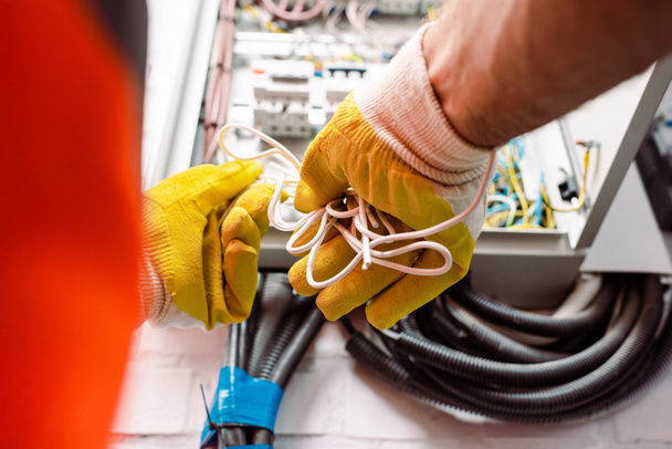 Vista recortada del electricista en guantes sosteniendo cables cerca de la caja eléctrica
 - Foto, imagen