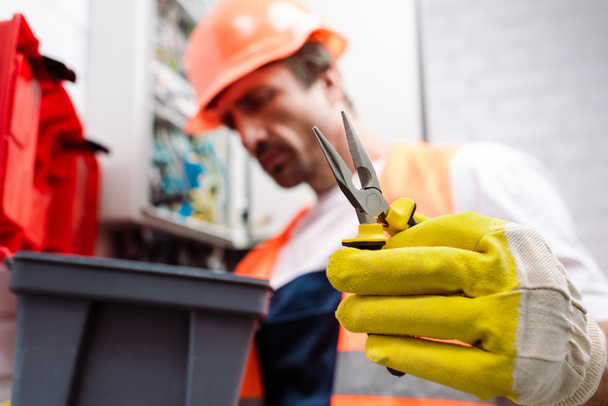 Selective focus of electrician in hardhat holding pliers near toolbox  - Photo, Image
