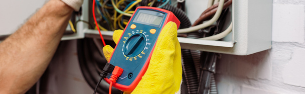 Panoramic crop of electrician using multimeter near electrical distribution box - Photo, Image
