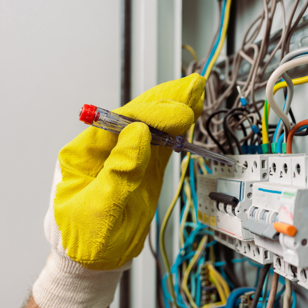 Gesneden weergave van elektricien in handschoen met behulp van schroevendraaier tijdens het repareren van elektrische distributiekast - Foto, afbeelding