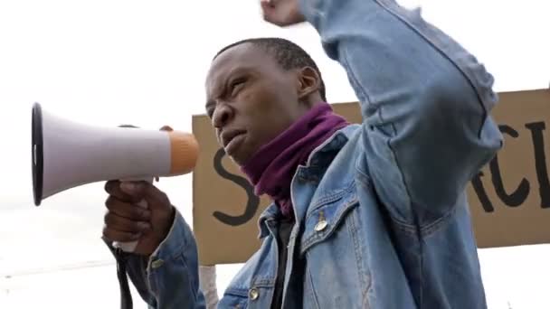 At a protest against racism dark-skinned young protester shouts angrily in megaphone. - Materiał filmowy, wideo