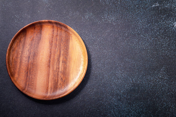 Round wooden plate on a black background. Copy space - Photo, Image