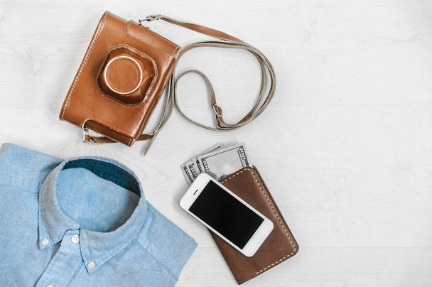 одежда для путешественников на белом деревянном фоне с пленочной камерой, паспортная рубашка и деньги - Фото, изображение
