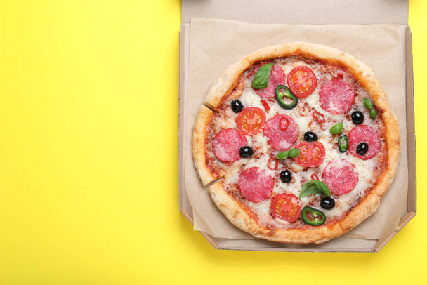 Delicious pizza Diablo in cardboard box on yellow background, top view. Space for text - Foto, afbeelding