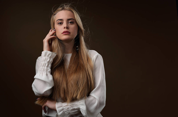 Portrait of a beautiful girl with long hair in a white blouse on a dark background - Foto, Imagen