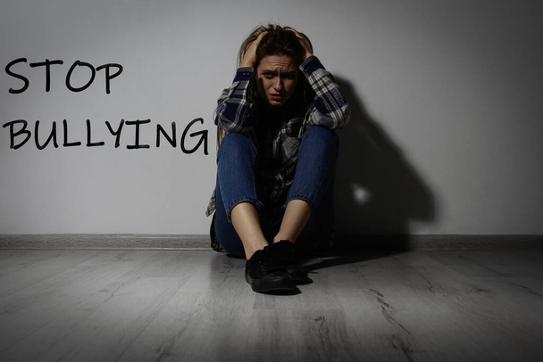 Message STOP BULLYING and abused teen girl crying near white wall - Photo, image