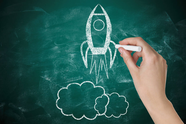 Business startup concept. Woman drawing rocket on chalkboard, closeup - 写真・画像