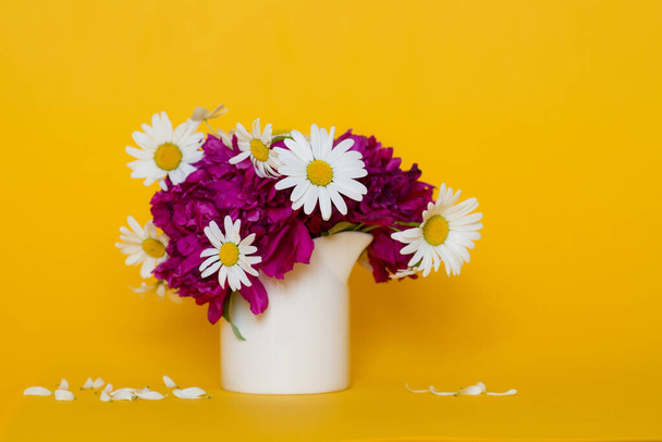 Bouquet of flowers from peonies and daisies in a vase on a yellow background. Mocap. - Foto, imagen