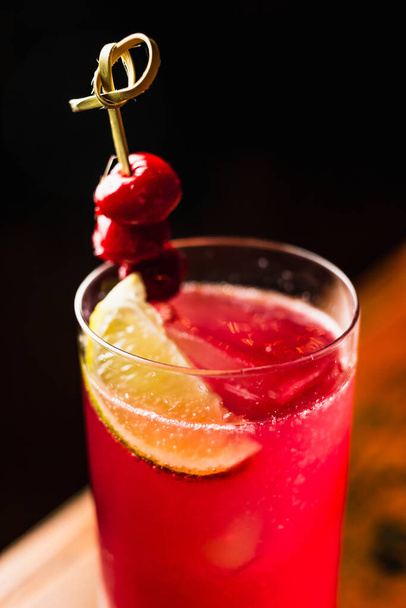 A red cocktail in a highball glass garnished with lemon and cherries - Foto, immagini