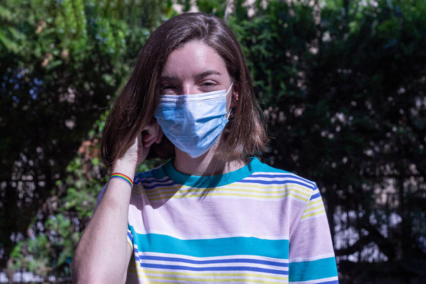 Έφηβη που κρατάει τη μάσκα της αφού τη βγάλει, χαρούμενη που μπορεί να βγει έξω και να σεβαστεί τα μέτρα ασφαλείας. Έννοια του covid και πρόληψη της υγείας - Φωτογραφία, εικόνα