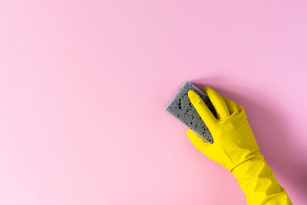Рука в жёлтой резиновой перчатке с чистящей губкой на розовом фоне
 - Фото, изображение