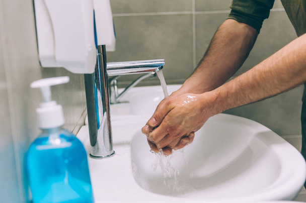 A young man washing his hands with liquid soap in the toilet, on the background of the washbasin. Stop COVID-19. - Φωτογραφία, εικόνα