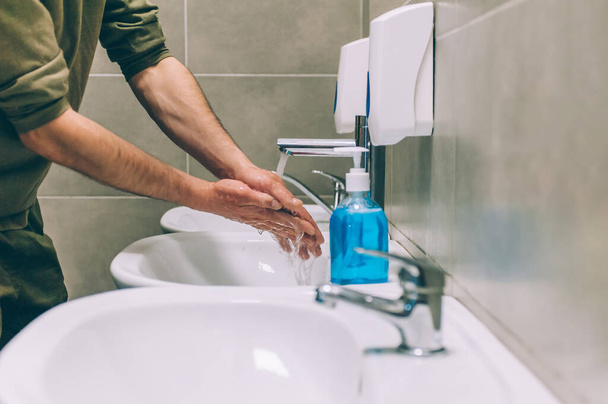 A young man washing his hands with liquid soap in the toilet, on the background of the washbasin. Stop COVID-19. - Fotografie, Obrázek