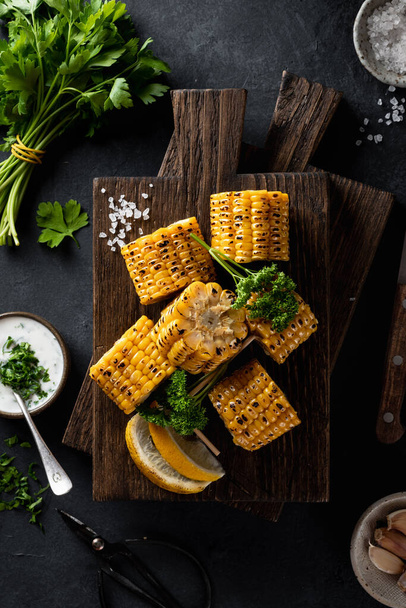 grilled corn on cob on a wooden cutting board on a dark background, top view - Foto, Imagem
