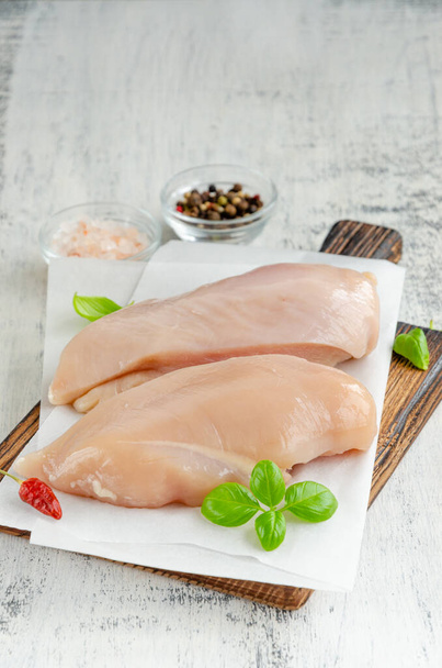 薄い木製の背景にバジルや他のスパイスとまな板の上に生の鶏の胸肉。健康食品。縦・横・縦 - 写真・画像