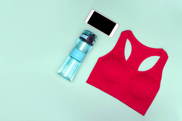 Sports top, water bottle, phone on a turquoise background. - Photo, Image