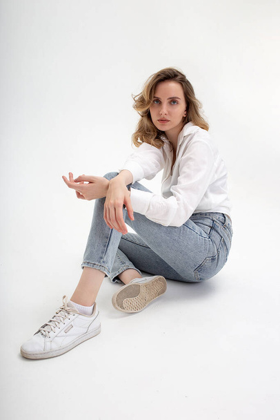 young cute pensive caucasian girl posing in white shirt, blue jeans at studio - Photo, Image