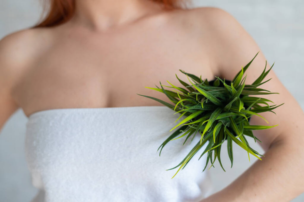 Close-up. Cropped. A woman in a white towel holds an armpit in a pot with a plant simulating unwanted vegetation on her body. Depilation. Hair removal in the armpit area. Smooth skin after epilation. - Foto, afbeelding