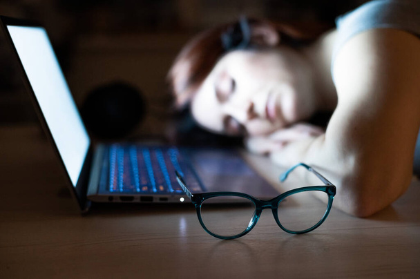 Der erschöpfte Mitarbeiter machte Überstunden und schlief an seinem Schreibtisch ein. Deadline Arbeiten in der Nacht mit einem Laptop. Der Student bereitet sich auf die Prüfung vor. - Foto, Bild