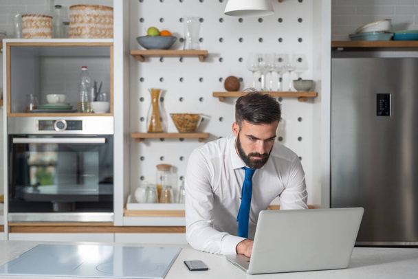 Young bearded businessman standing in the kitchen and check the company work list for his new business plan and  project on his laptop computer - Foto, Bild