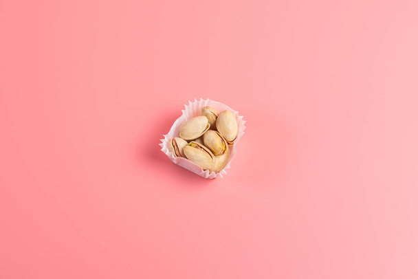A serving of pistachios in a paper muffin cup on a pink background. - Foto, afbeelding
