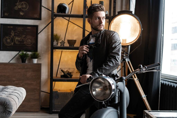 Stylish young man in leather jacket sitting on motorbike. - 写真・画像