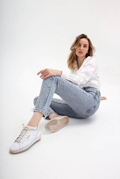 giovane ragazza caucasica pensosa carina in posa in camicia bianca, jeans blu in studio - Foto, immagini