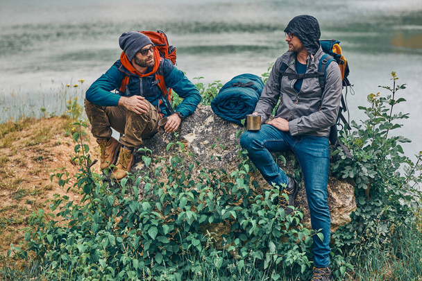 美しい自然を眺めながらハイキングから休んでいる2人のハンサムな男性とコーヒーを飲む. - 写真・画像