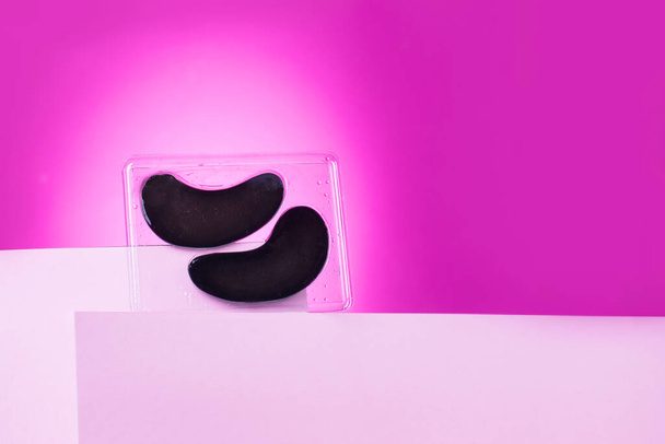 Μαύρα μπαλώματα ματιών στέκονται στο βάθρο, σε ένα φωτεινό ροζ φόντο. Ένα μέρος για μηνύματα. Καλλυντικά και προϊόντα περιποίησης - Φωτογραφία, εικόνα