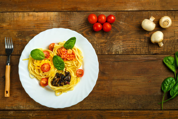 Plate of pasta nests stuffed with assorted pasta paste, cheese with cherry and fried mushrooms next to vegetables. - Photo, Image
