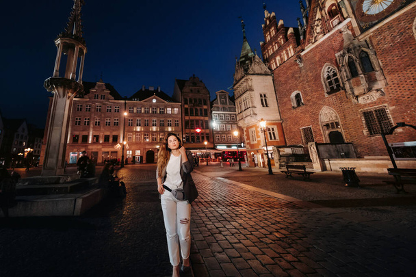 a romantic girl walks in the old town of Wroclaw in the late evening.Walk of a woman in trousers and jacket in the old town of Poland. - Photo, image