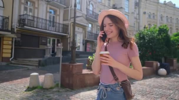 Mooie jonge vrouw toerist met afhaalkoffie in het centrum van de stad praten aan de telefoon - Video