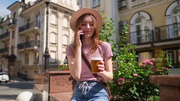 Красивая молодая туристка с кофе на вынос в центре города разговаривает по телефону - Кадры, видео