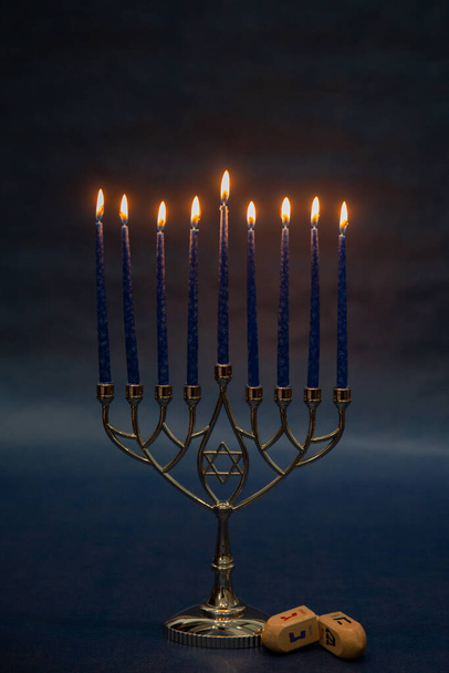 Burning blue candles on a Jewish menorah at Hanukkah with a dreidel on a dark blue background - Photo, Image