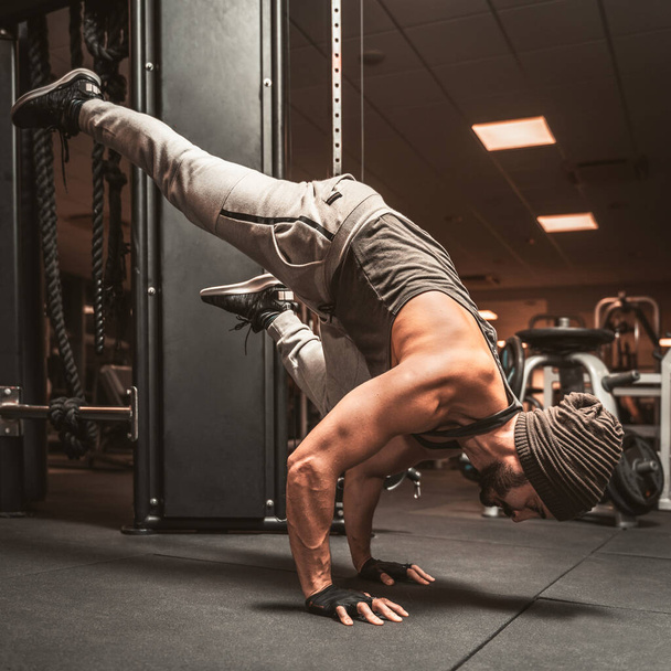 Un homme sportif barbu dans la salle de gym fait des exercices de yoga. Position sur les bras. Avantages mentaux de yoga. Ardha Bakasana ou corbeau pose.. Une position d'équilibrage des jambes. - Photo, image