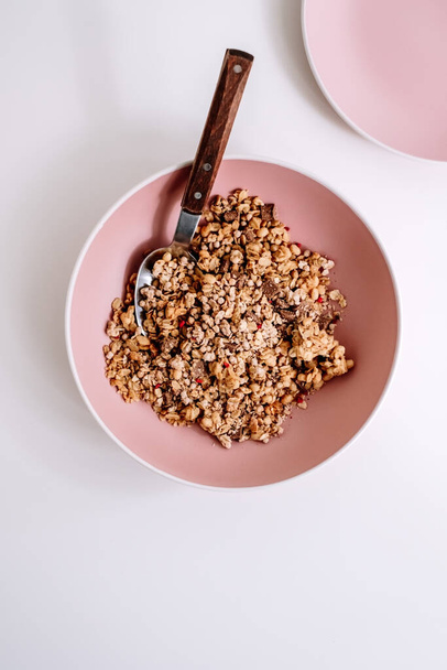 Granola muesli with pieces of chocolate in a pink plate on a white table. Healthly food, breakfast concept. High quality photo - Foto, imagen